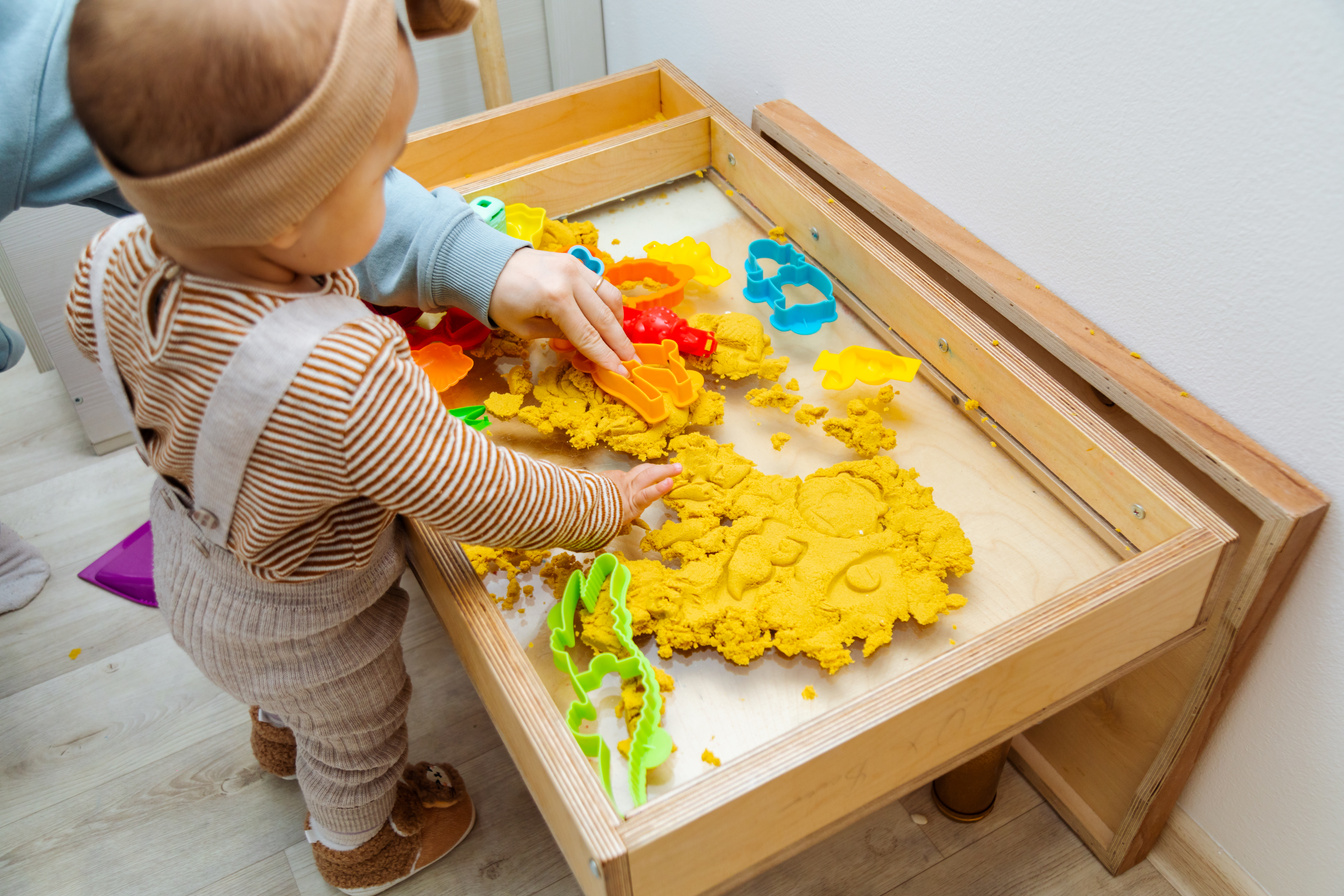 Toddler playing kinetic sand with plastic shapes