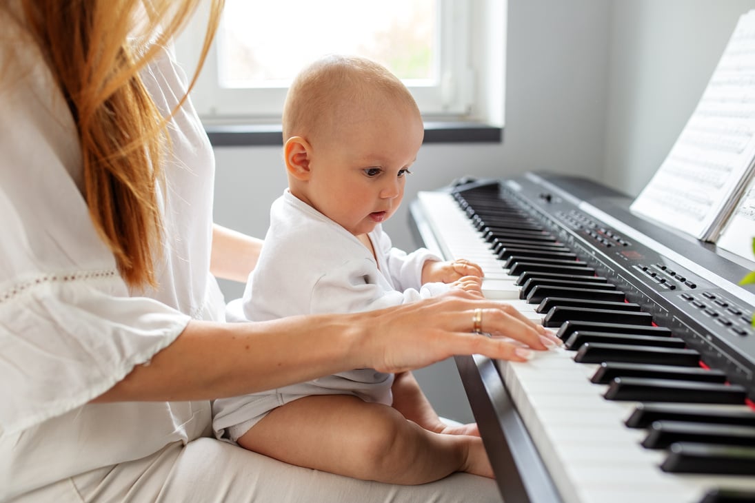 Mother and baby daughter playing piano, close up. Baby development. Sensory experience. Early years