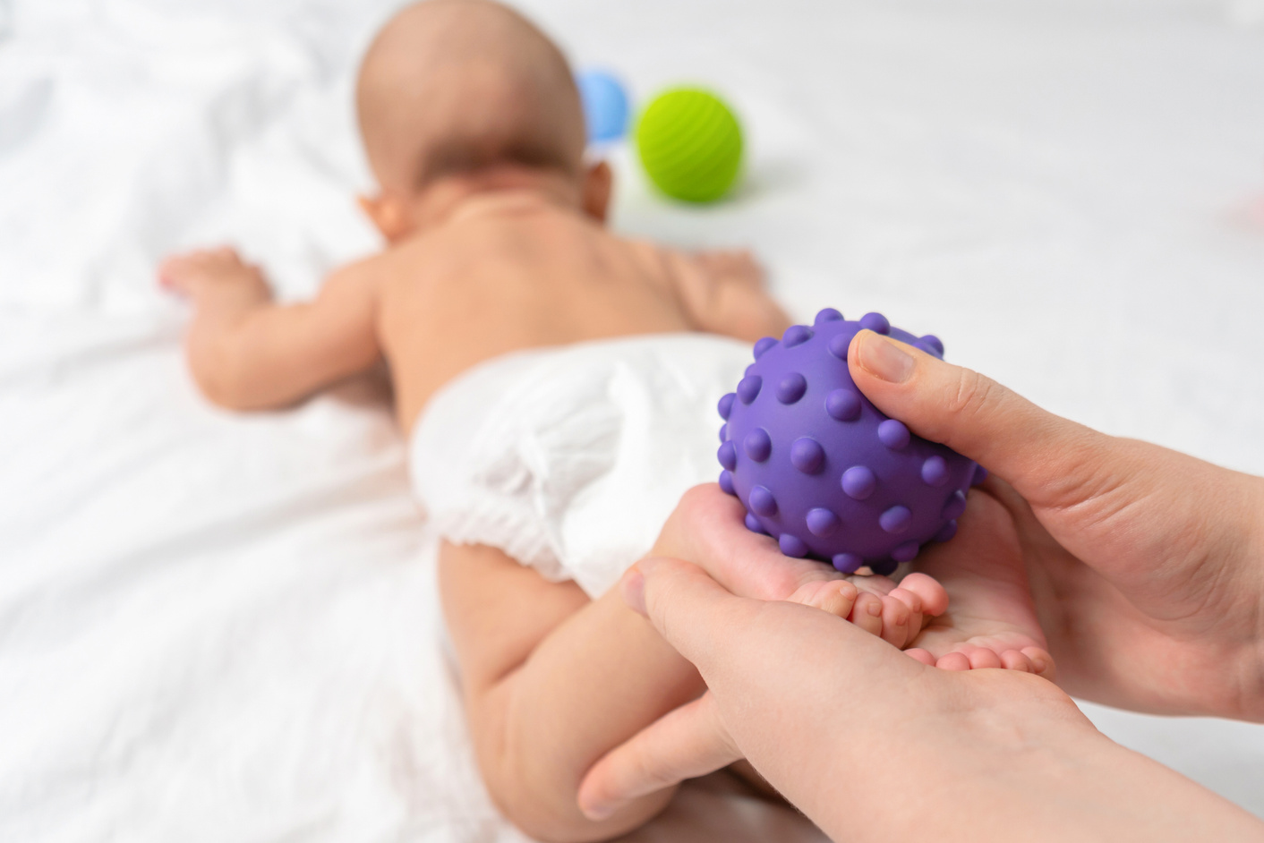 Mom massage the baby's feet with a purple rubber ball. Baby massage. Selective focus